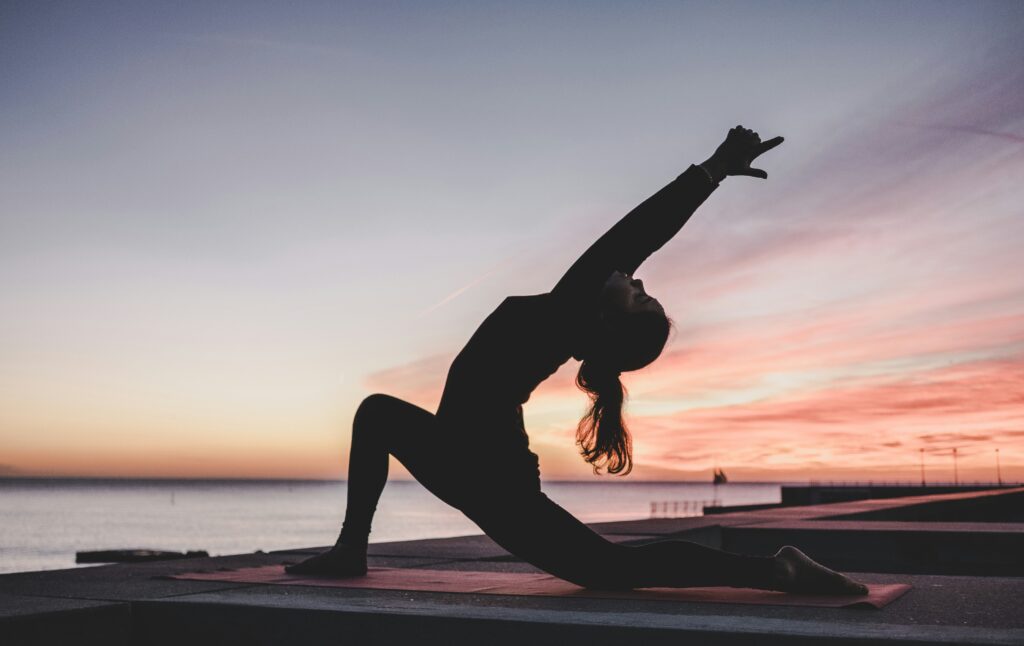 Woman practicing sunrise yoga outdoors as a sober activity during travel