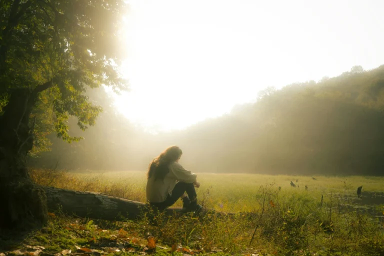 Girl reflecting outdoors on a calm, misty morning overlooking a field, symbolizing early sobriety and personal growth