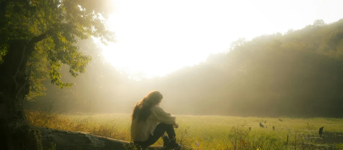 Girl reflecting outdoors on a calm, misty morning overlooking a field, symbolizing early sobriety and personal growth